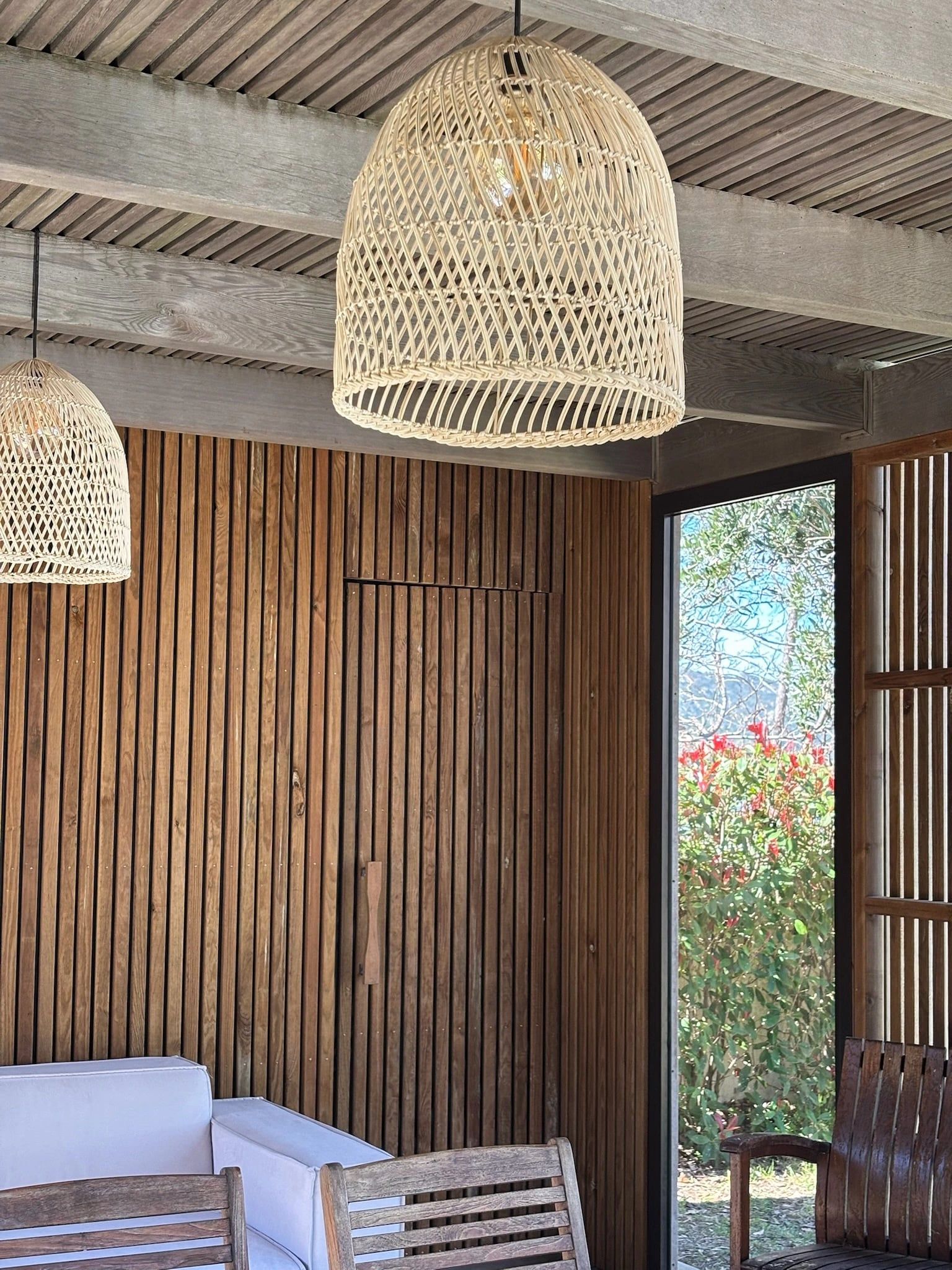 Mur habillé de tasseaux de bois avec porte dérobée, sous un plafond à lames et suspensions en rotin
